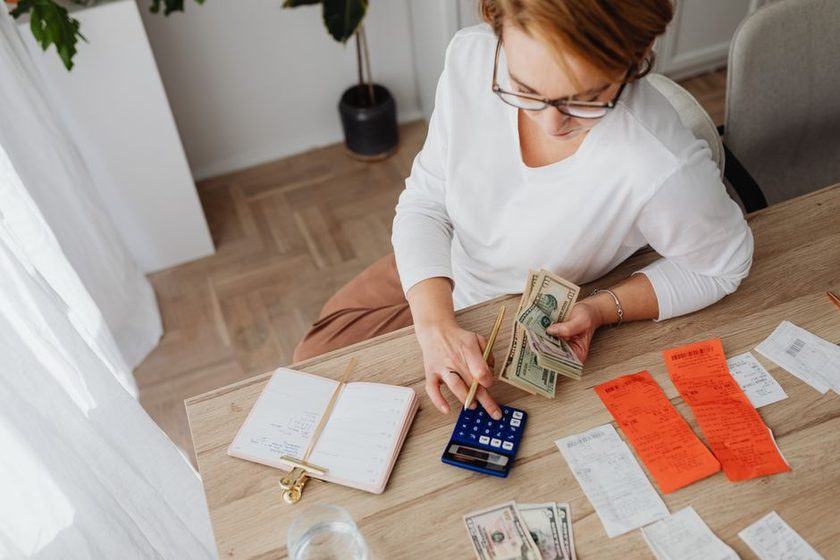 Mulher usa calculadora e organiza recibos e notas de dinheiro numa mesa de escritório em casa.