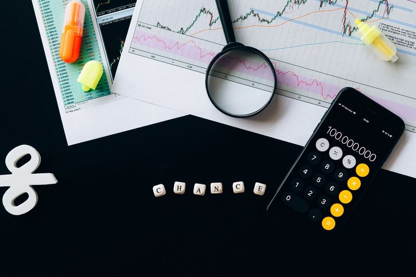 Calculadora com um valor alto na tela ao lado de gráficos financeiros impressos e uma lupa.